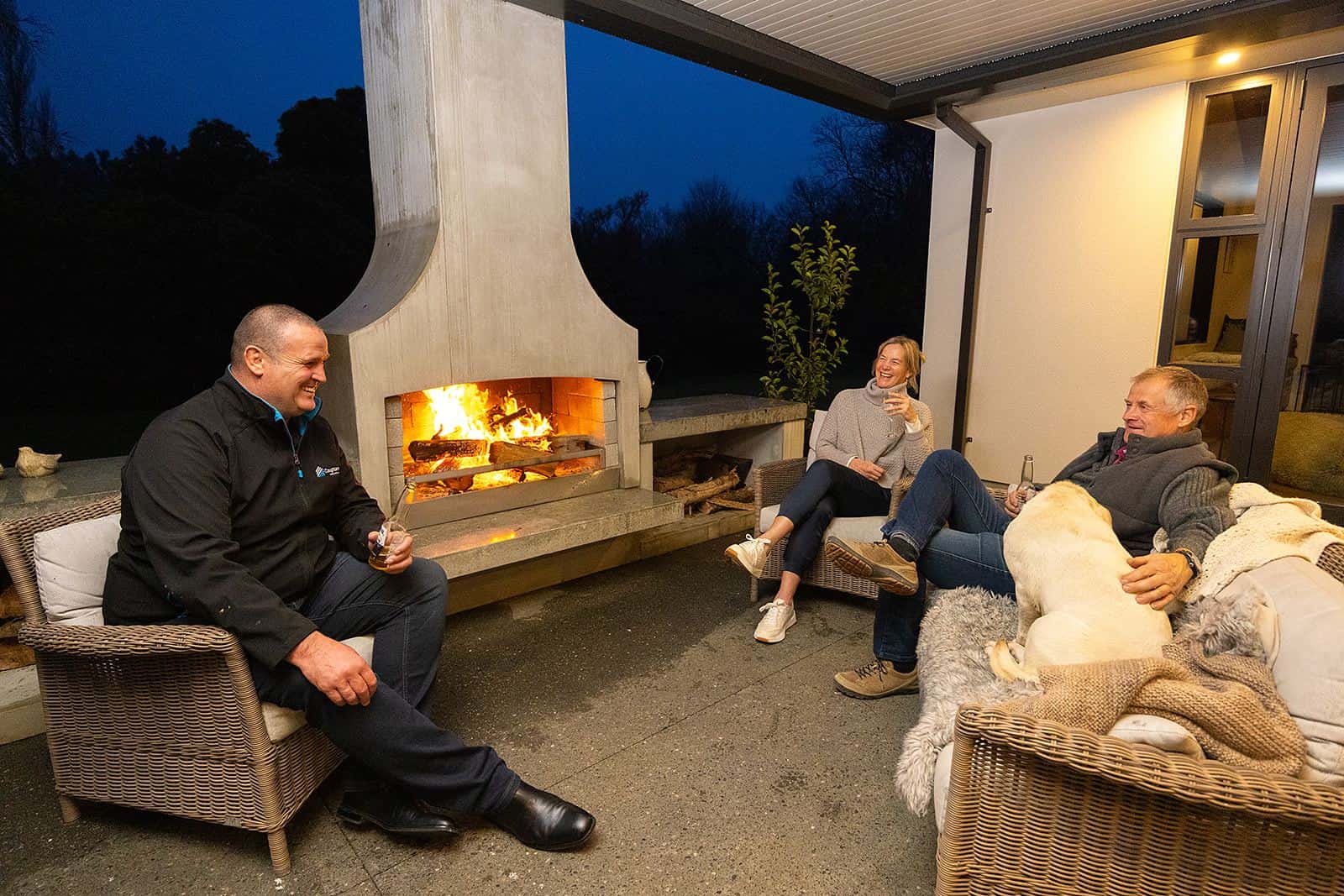 Pat Coughlan talking with clients beside the lit outdoor fireplace at the Parnassus homestead at dusk.