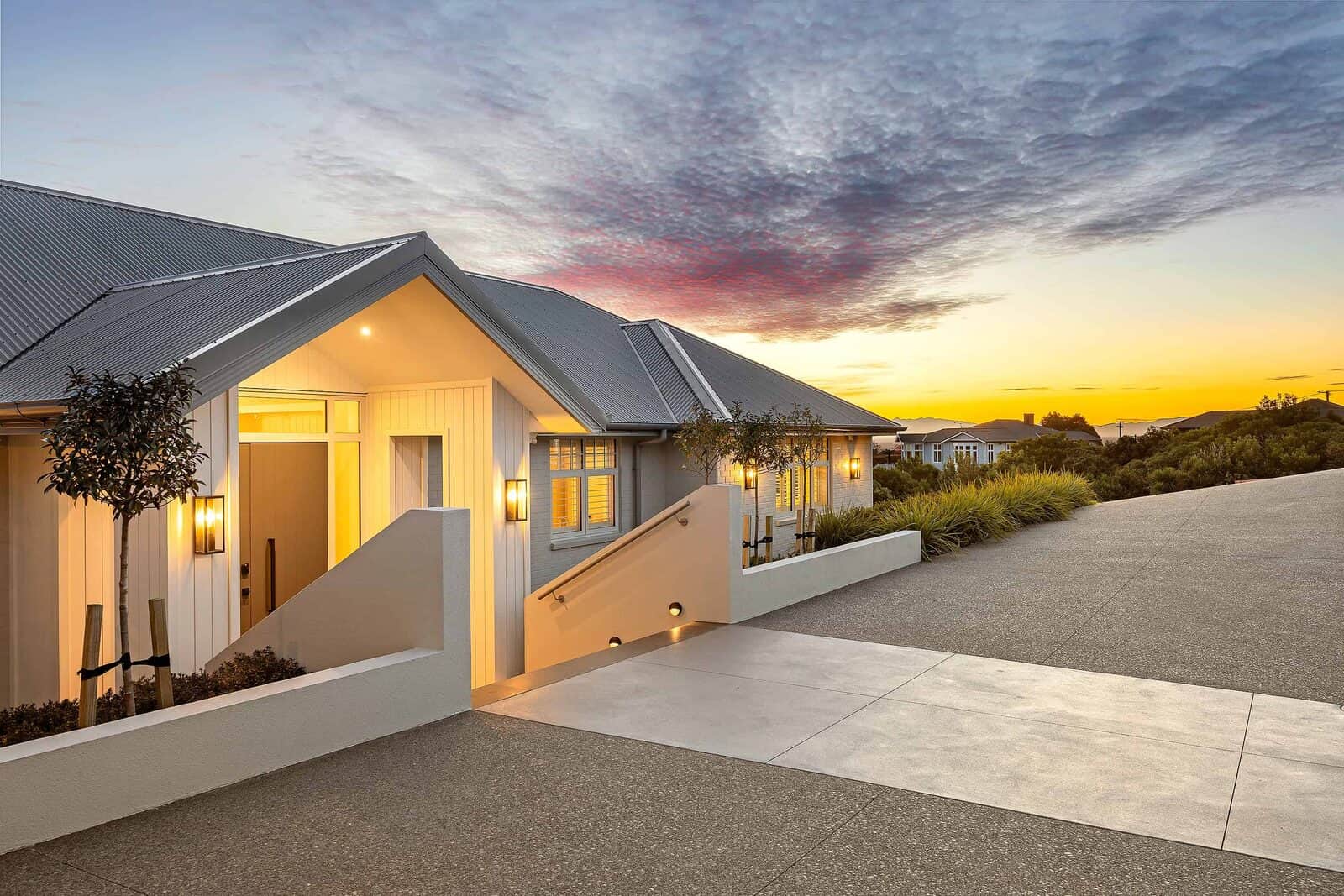 Front elevation of the Port Hills hillside home at dusk, with the gabled roofline lit against the sky.